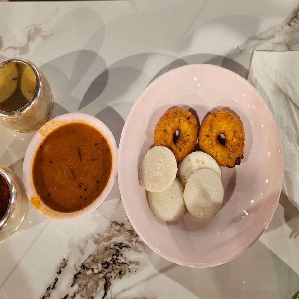South Indian breakfast platter with idlis, vadas, sambar, chutneys, and utensils on a marble table.