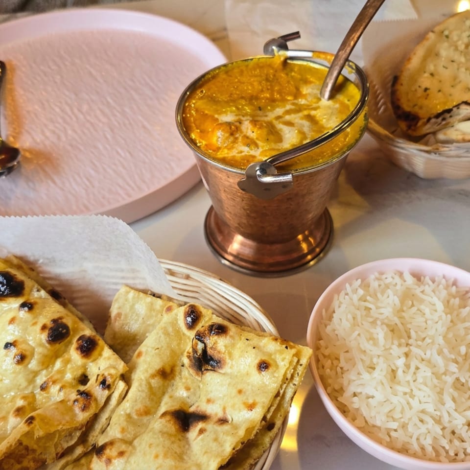 Indian meal featuring naan bread, basmati rice, and creamy curry served in a copper bowl on a marble table.