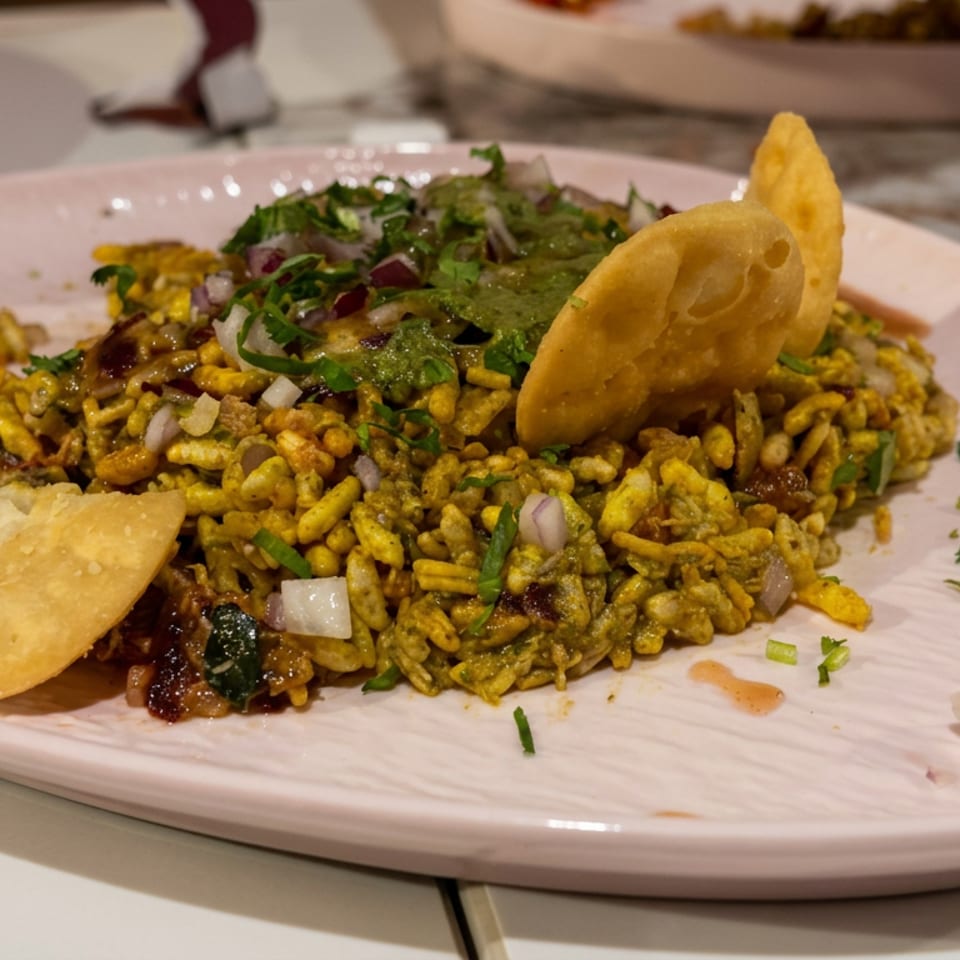 Indian bhel puri chaat topped with cilantro, onions, chutneys, and crisp papdi on a plate.