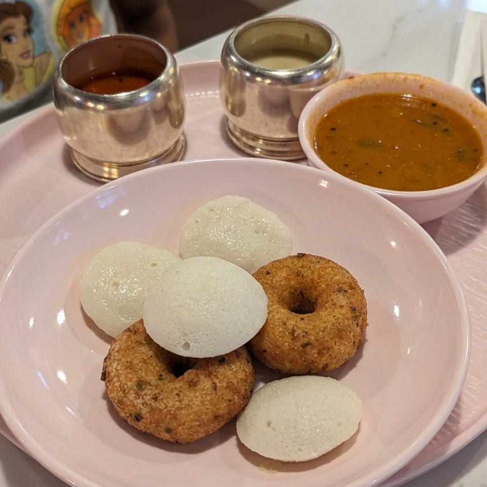 Plate of South Indian idlis and medu vadas served with sambar and chutneys on a pink tray.